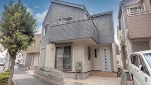 A two-story residential building with a flat roof, a front porch, and a visible garage door. - Iris Tokyo ２ (Tokyo)