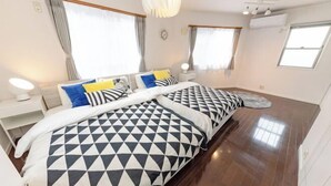 A hotel room with two beds, a wooden floor, a white wall clock, and a window with curtains. - Iris Tokyo ２ (Tokyo)