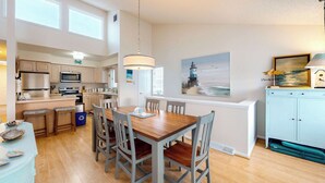 Una cocina amplia con electrodomésticos modernos, un comedor con sillas de madera y vistas al mar a través de una ventana.