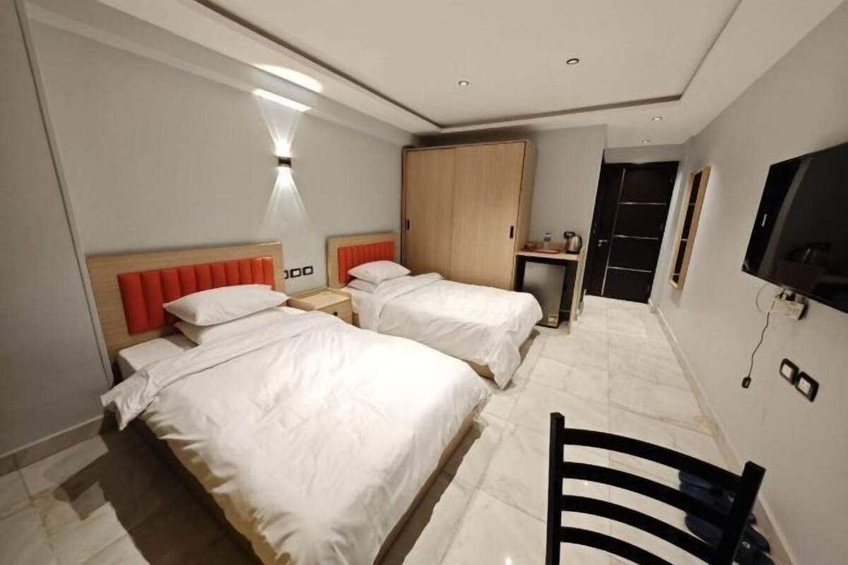 A hotel room with two beds, a wardrobe, a desk, a chair, and a TV.
