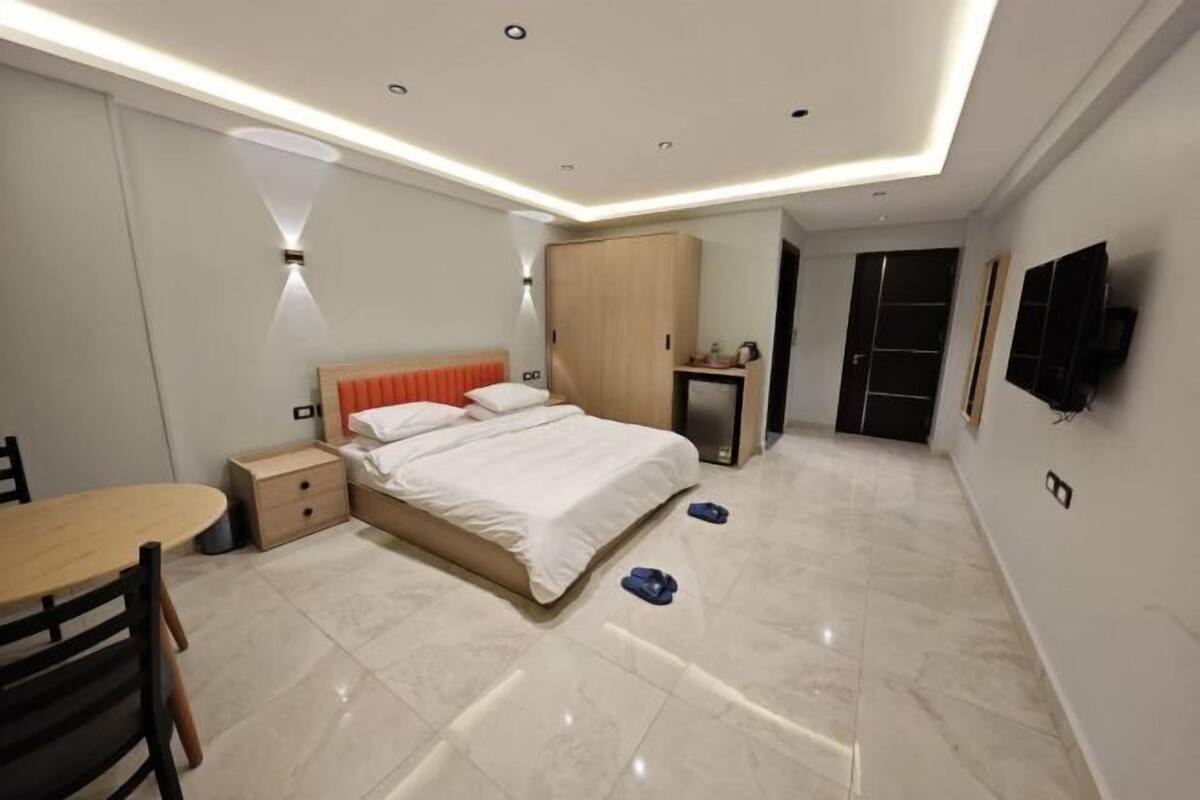 A modern bedroom with a bed, bedside table, wardrobe, and a TV mounted on the wall.