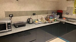 Una cocina con microondas, hervidor y diversos alimentos sobre la encimera.