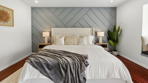 Une chambre moderne avec un grand lit, deux tables de chevet avec des lampes, un panneau décoratif mural et une plante en pot.