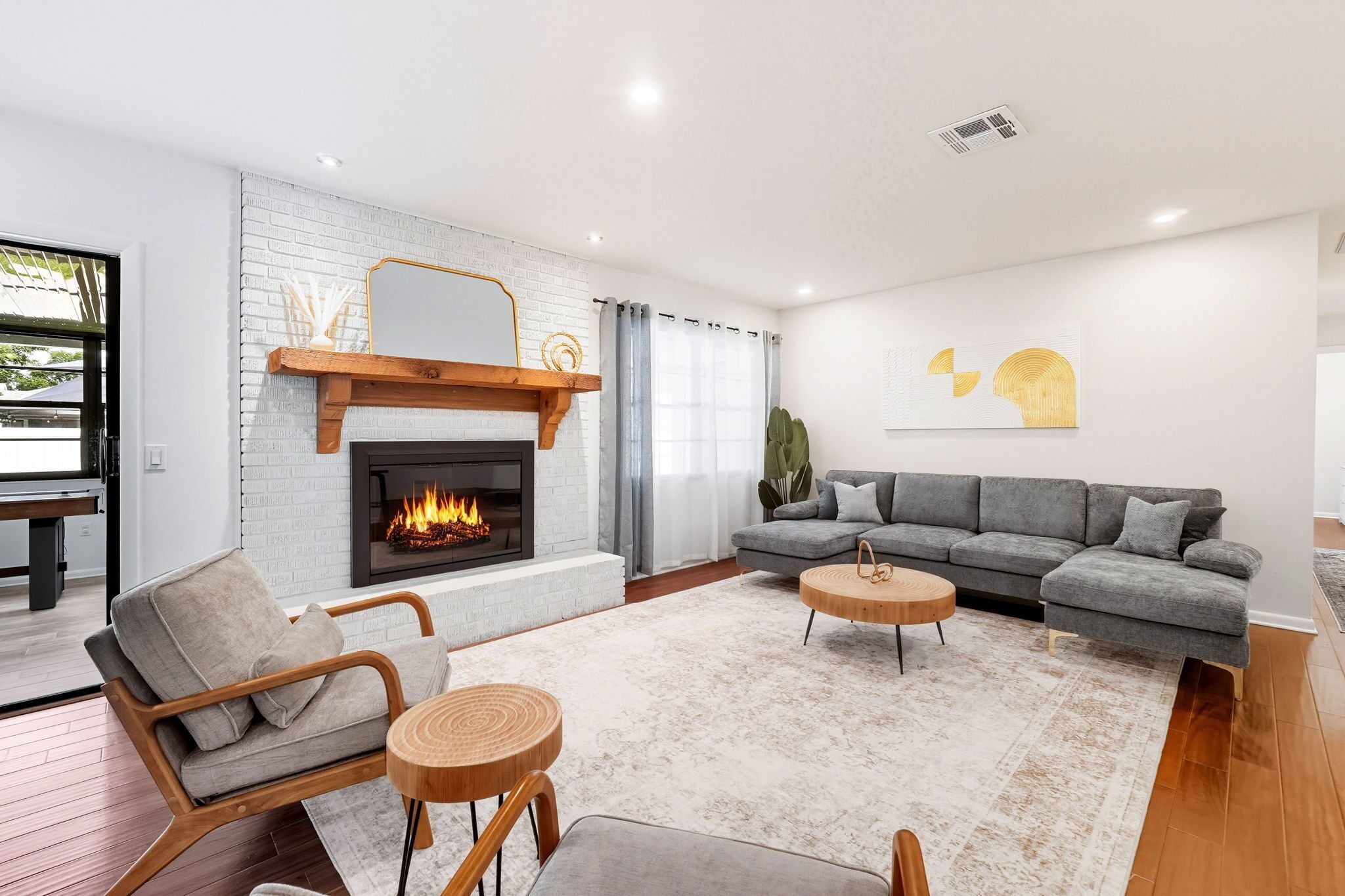 A modern living room with a fireplace, grey sofa, wooden chairs, and a round coffee table.