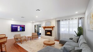 Un salon moderne avec une cheminée, un téléviseur à écran plat fixé au mur et une grande fenêtre avec des rideaux.