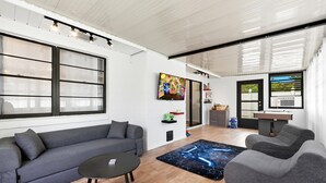 Un salon moderne avec un canapé gris, une table basse ronde et une table de jeux.