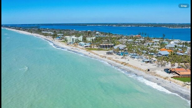 Vista aérea de un complejo turístico frente a la playa, con propiedades en primera línea de mar, aguas azul cristalino y una vista distante del océano.