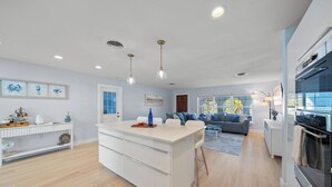 Una cocina moderna con una isla central, muebles blancos y una zona de comedor con sofá y mesa de centro.