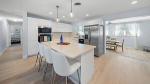 Una cocina moderna con armarios blancos, electrodomésticos de acero inoxidable y una isla central con taburetes de bar.