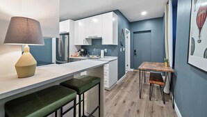 A modern kitchen with white cabinets, a wooden dining table, and a bar area with stools. - The Luxe Pearl Residences 8ppl (Columbus)