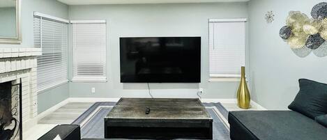 A living room with a flat-screen TV mounted on the wall, a fireplace, and a sofa.