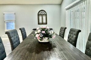 A dining room with a long wooden table, six tufted chairs, and a floral centerpiece.