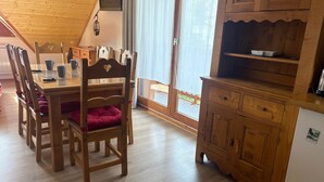 A wooden dining table with chairs, a kitchen area with wooden cabinets, and a window with curtains. - 3-bedroom apartment for 6 in Saint-François-Longchamp (Saint-François-Longchamp)