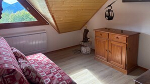 A bedroom with a sloped ceiling, a wooden cabinet, a bed with patterned bedding, and a wall-mounted lamp. - 3-bedroom apartment for 6 in Saint-François-Longchamp (Saint-François-Longchamp)