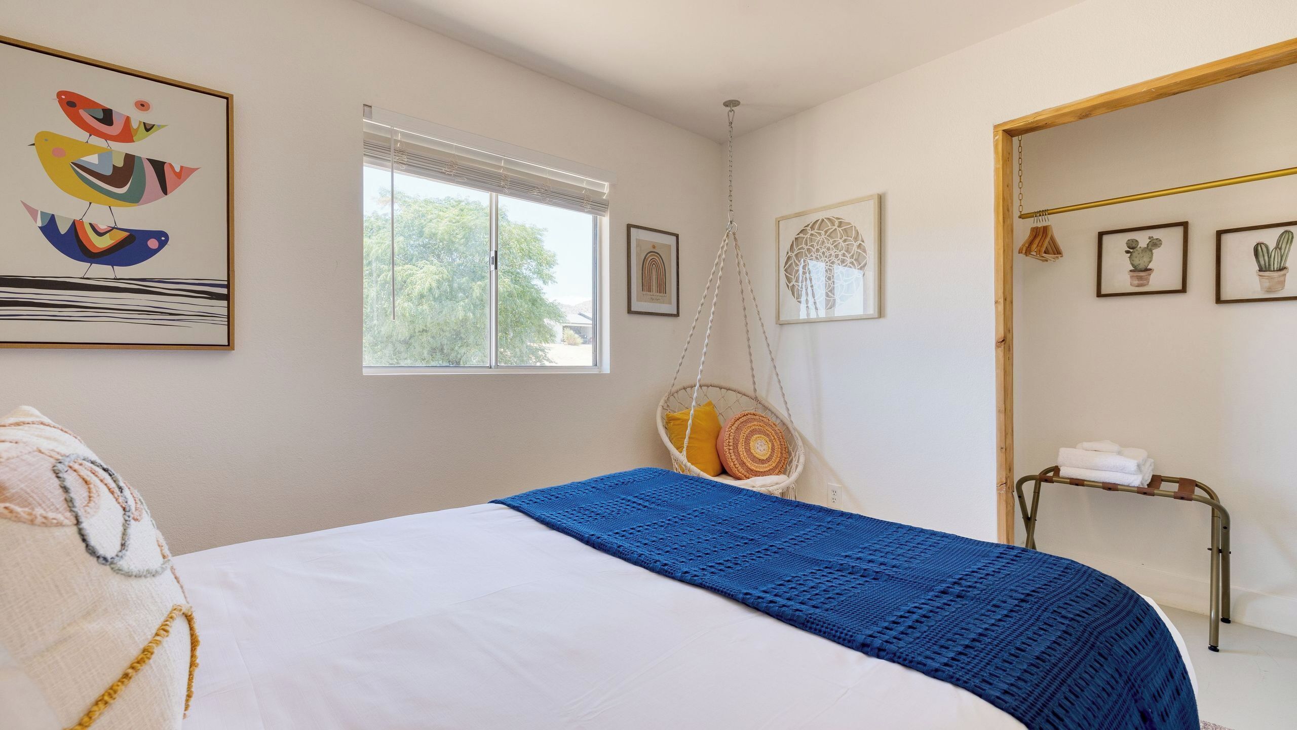 Ein Schlafzimmer mit Bett, Hängesessel, Fenster und Wandbildern.
