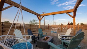 A covered outdoor seating area with swing chairs, a fire pit, and a wooden pergola.