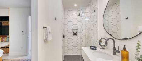 A modern bathroom with a hexagonal tile backsplash, a large mirror, a sink with a faucet, and a shower area.