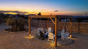 Een houten pergola met hangstoelen en een tafel, omgeven door woestijnplanten.