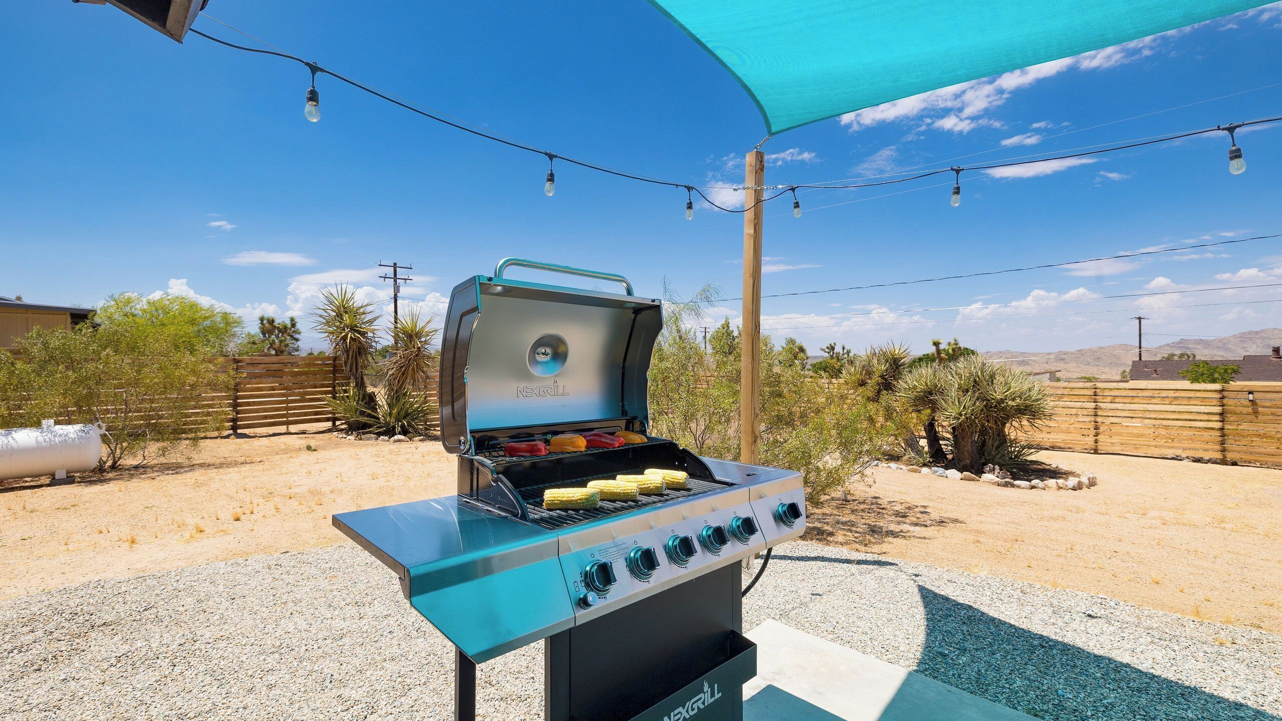 Una parrilla para barbacoa con diseño azul y negro, ubicada al aire libre con un cielo despejado y vegetación desértica en el fondo.