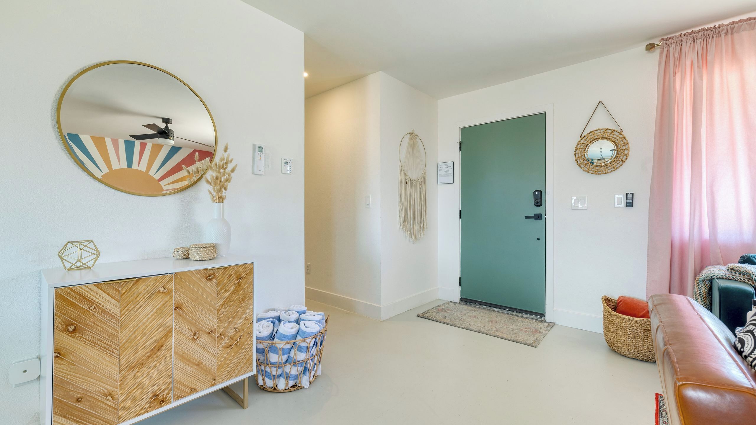 Una sala de estar moderna con un mueble de madera, un espejo redondo, una puerta verde y una cortina rosa.