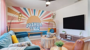 Een woonkamer met een kleurrijke muurschildering, een bank, een salontafel, een televisie en een hangstoel.