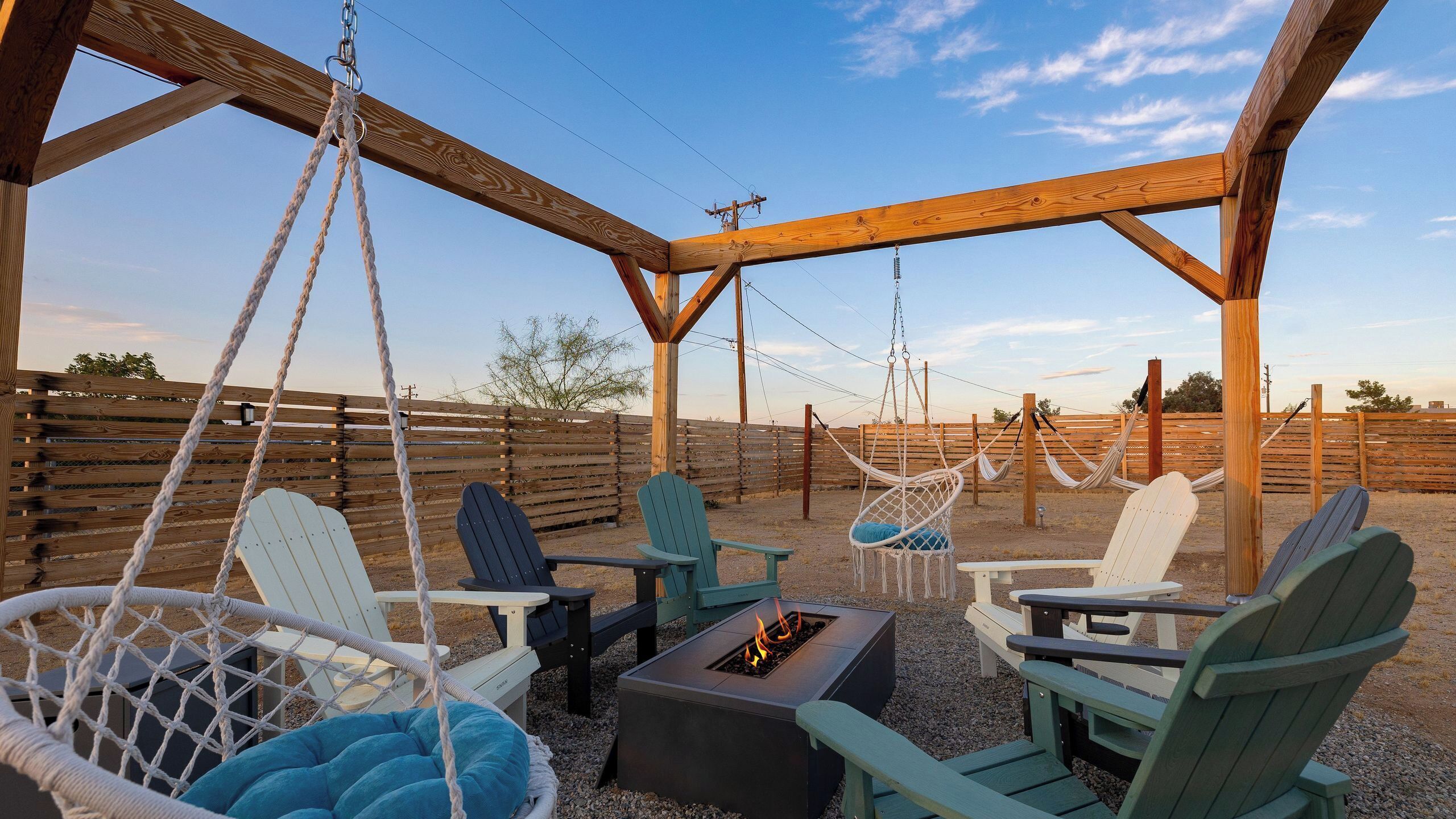 A covered outdoor seating area with swing chairs, a fire pit, and a wooden pergola.