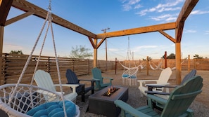 A covered outdoor seating area with swing chairs, a fire pit, and a wooden pergola.