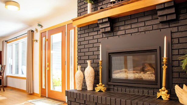 A fireplace with three candles, a framed picture above it, and a brick wall.