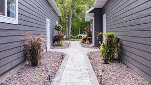 A pathway leading to a house with grey siding, surrounded by potted plants and a gravel driveway.