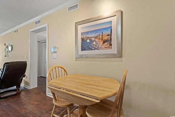 Uma área de refeições com mesa e cadeiras de madeira, um quadro na parede e uma poltrona de couro preto.