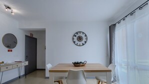 Ein stilvoller Essbereich mit einem Holztisch, weißen Stühlen, einer Wanduhr und einem großen Fenster mit durchsichtigen Vorhängen.
