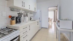 Eine moderne Küche mit weißen Schränken, einem Gasherd und einer Mikrowelle. Im Hintergrund ist ein Essbereich zu sehen.