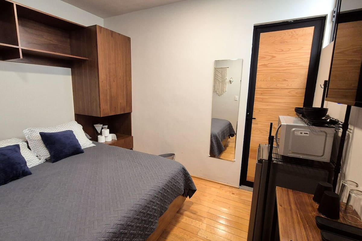 A bedroom with a bed, bedside tables, a mirror, and a kitchenette with a stove.