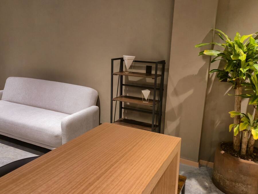 Una sala de estar con un sofá blanco, una mesa de centro de madera, una estantería metálica y una planta en maceta.