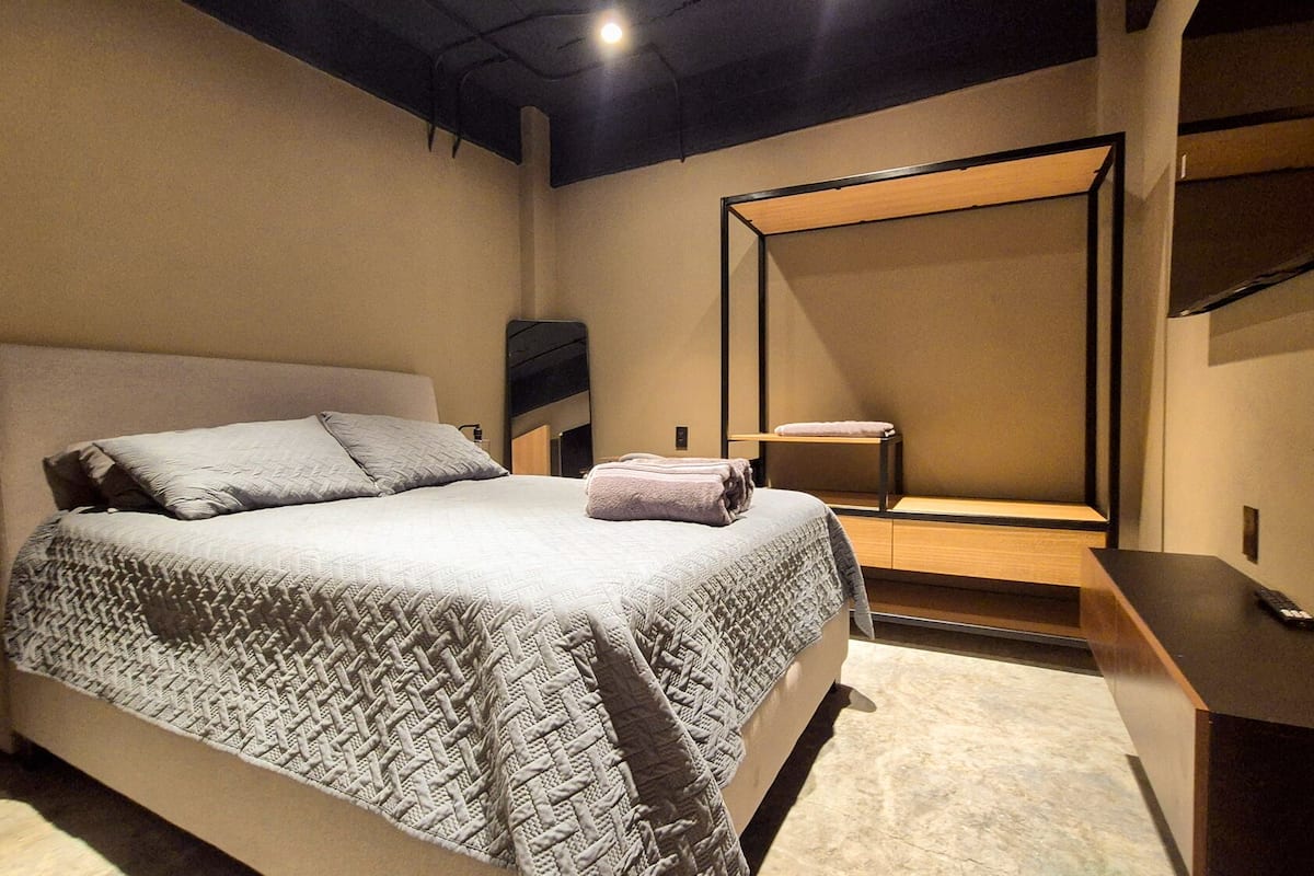 A modern bedroom with a large bed, a bedside table, a chair, a mirror, and a desk.