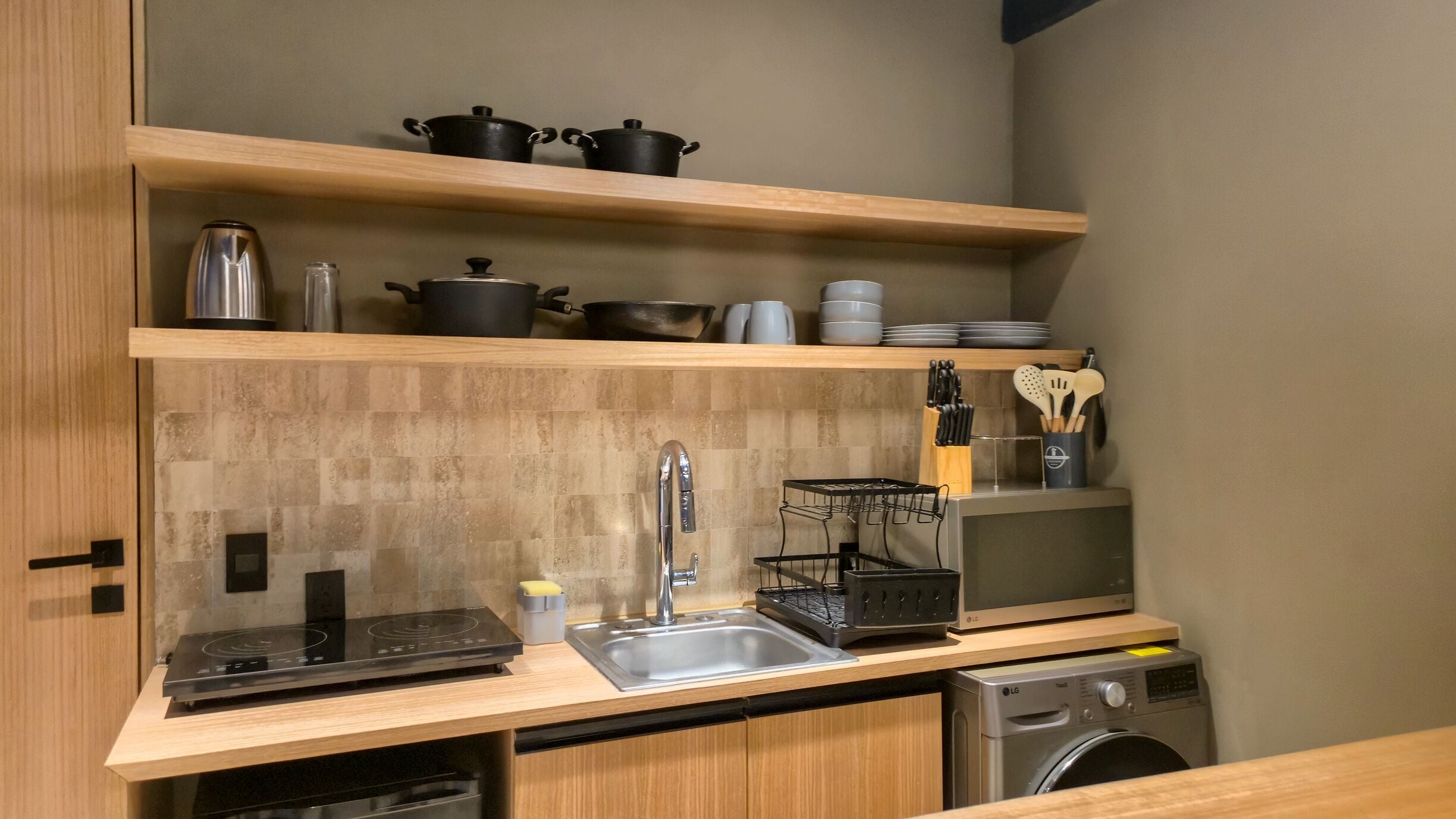 A compact kitchen with a built-in dishwasher, a sink, and wooden shelves above holding pots, pans, and kitchen utensils.