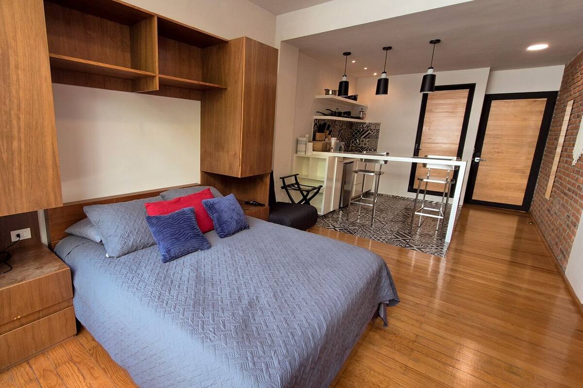 A modern bedroom with a large bed, built-in shelving, a desk, and a small kitchenette.