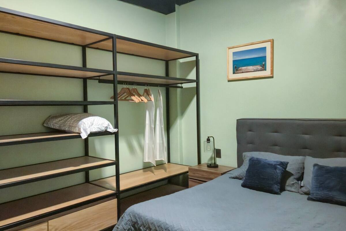 A room with bunk beds, a bed, a nightstand, a lamp, and a framed picture on the wall.