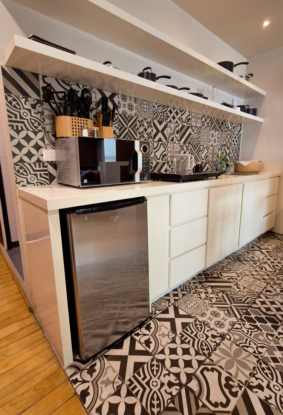 A compact kitchen with a built-in microwave, a small refrigerator, and a patterned backsplash.