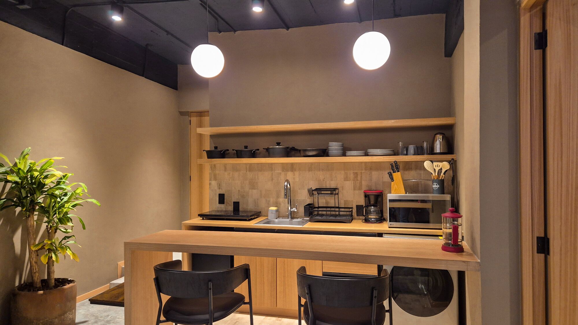 Una cocina compacta con encimera de madera, sillas negras, cafetera y microondas.