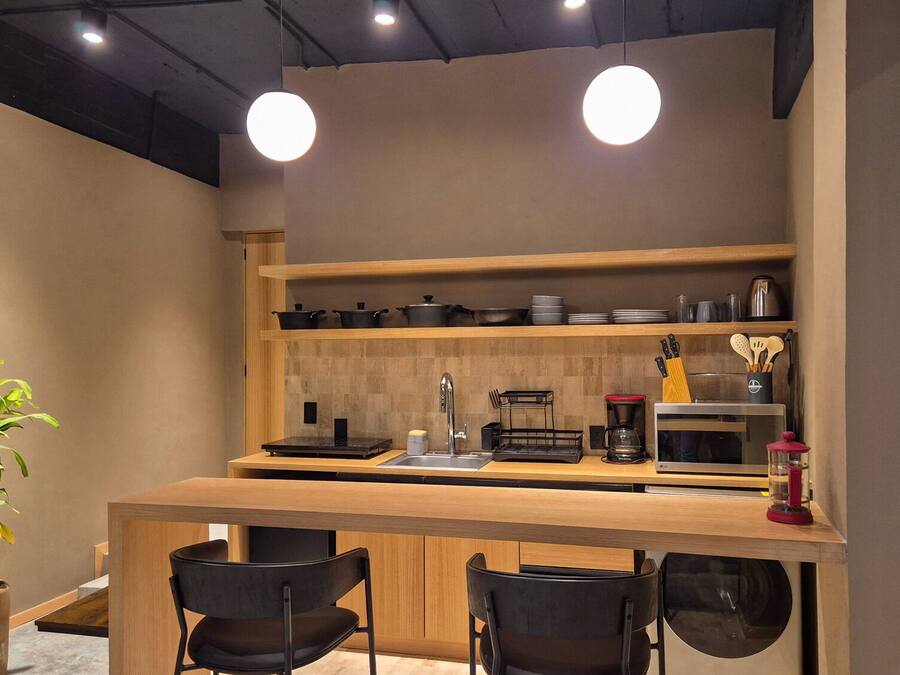 A compact kitchen with a wooden countertop, black chairs, a coffee maker, and a microwave.
