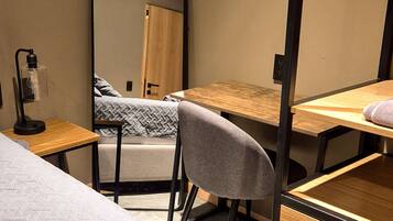 A compact room with a bed, a desk, a chair, and a mirror.
