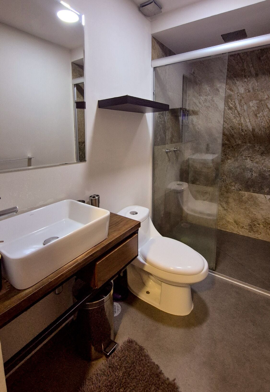 Un baño moderno con un lavamanos grande, inodoro y ducha con mampara de vidrio.