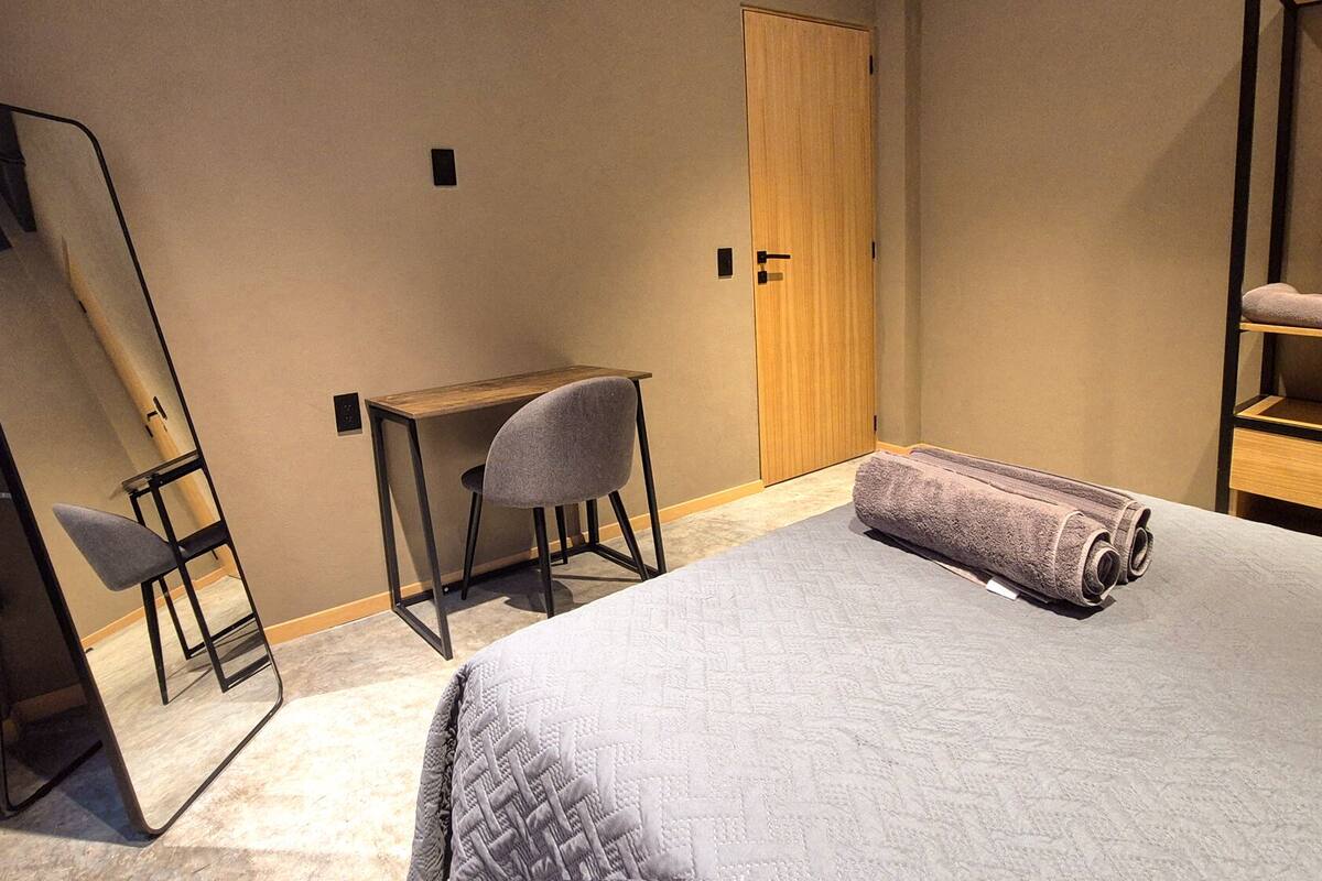 A bedroom with a bed, a desk, a chair, a mirror, and a wardrobe.