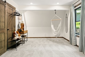 Una habitación con una mecedora colgante, un armario de madera, un escritorio con silla y una ventana con cortinas.