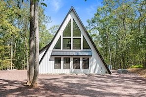 Eine weiße Holzhütte mit einem dreieckigen Dach, umgeben von Bäumen.