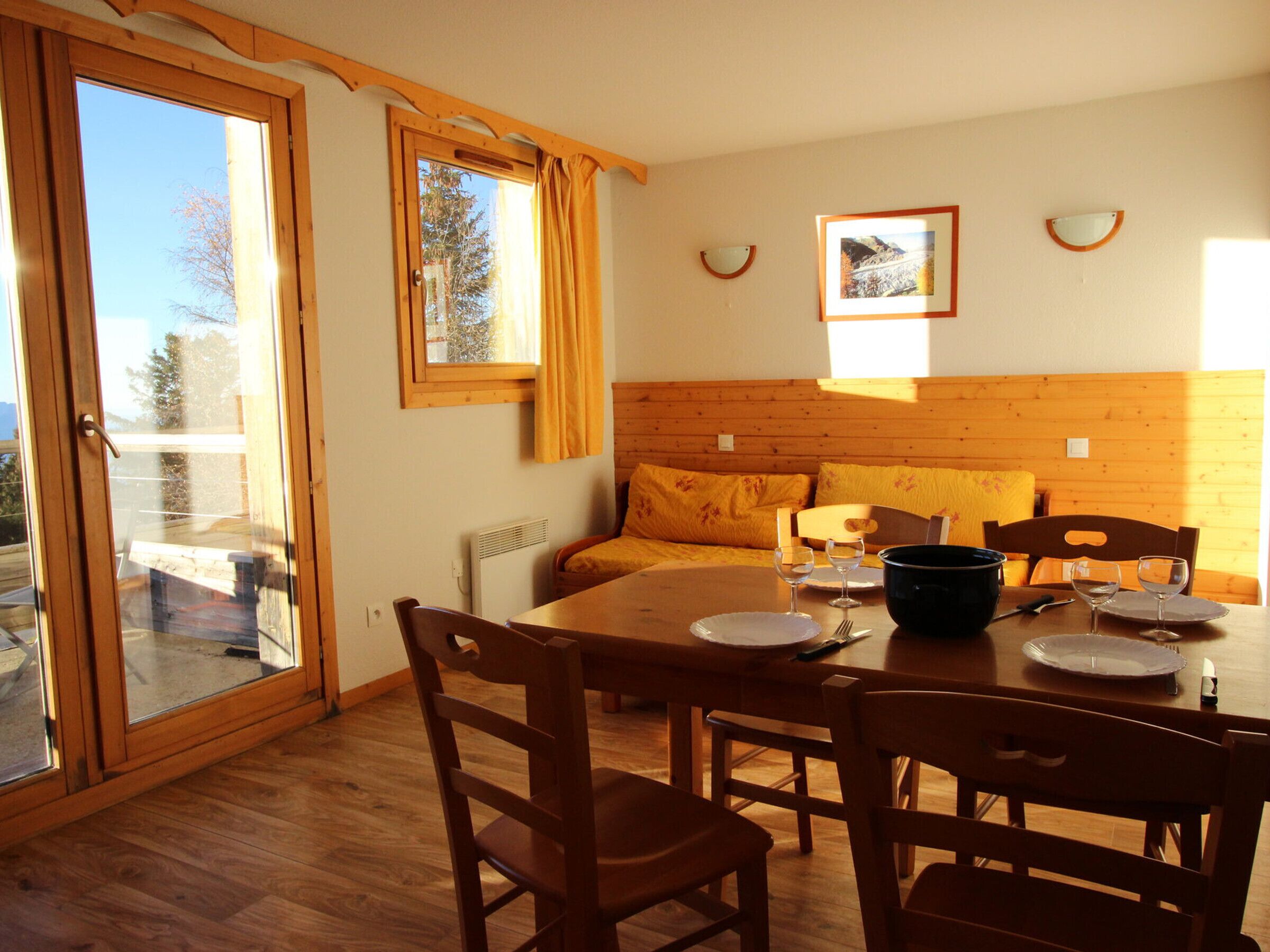 A dining area with wooden furniture, a table set for two, and a view through a glass door to the outside.