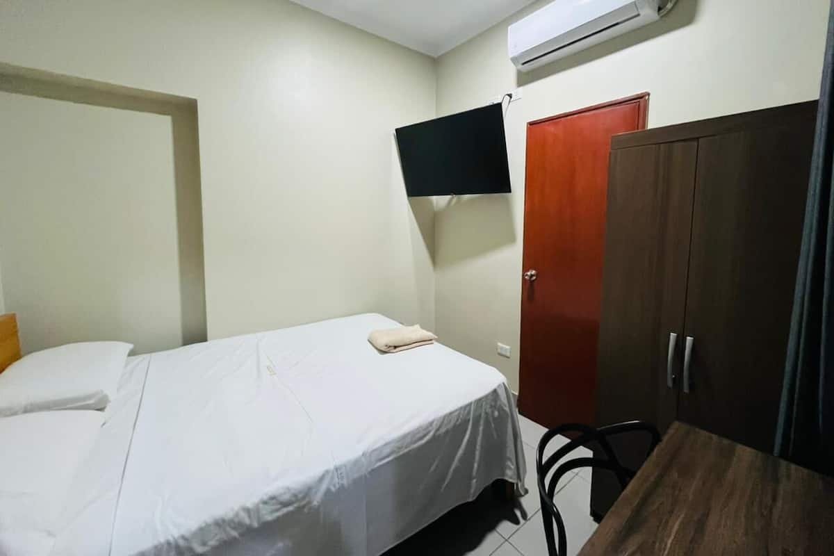 Ett hotellrum med en säng, en garderob, en platt-TV som är monterad på väggen och en luftkonditioneringsanläggning.