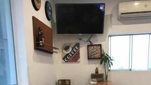 Un comedor con una mesa redonda de madera dispuesta para el desayuno, un televisor montado en la pared y una ventana con persianas.