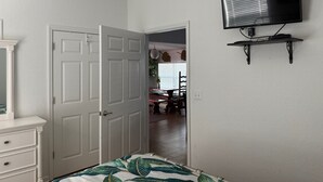 Ein Schlafzimmer mit einem Bett, einer weißen Kommode, einer geschlossenen Tür und einem an der Wand befestigten Fernseher.